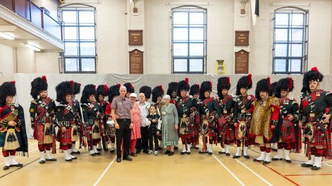 Raymond and his family is posing in front of Black Watch bagpipe band.