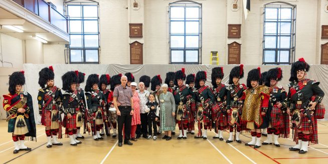 Raymond and his family is posing in front of Black Watch bagpipe band.