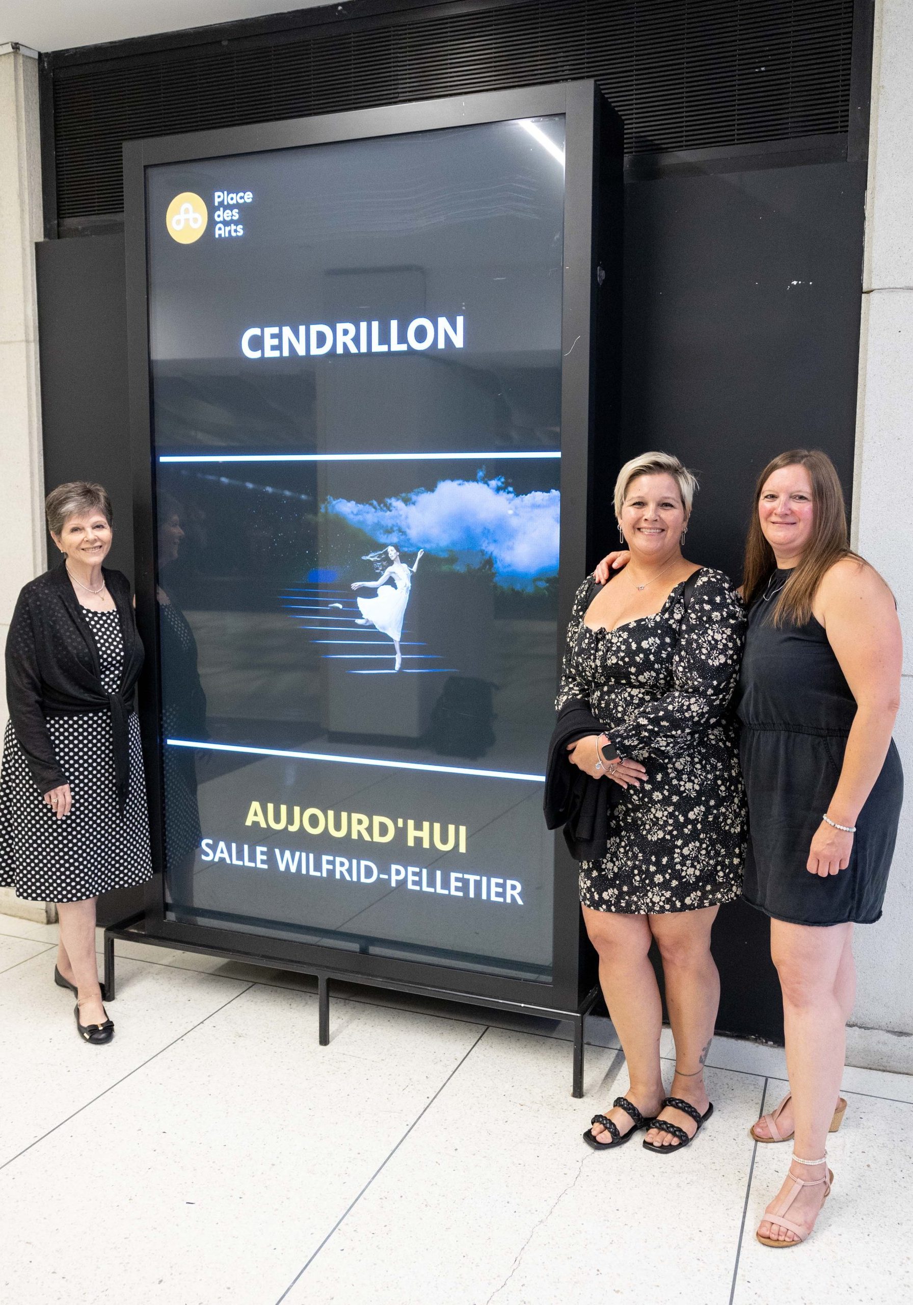 Lise stands in front of Les Grands Ballets Canadiens' poster with her daughters