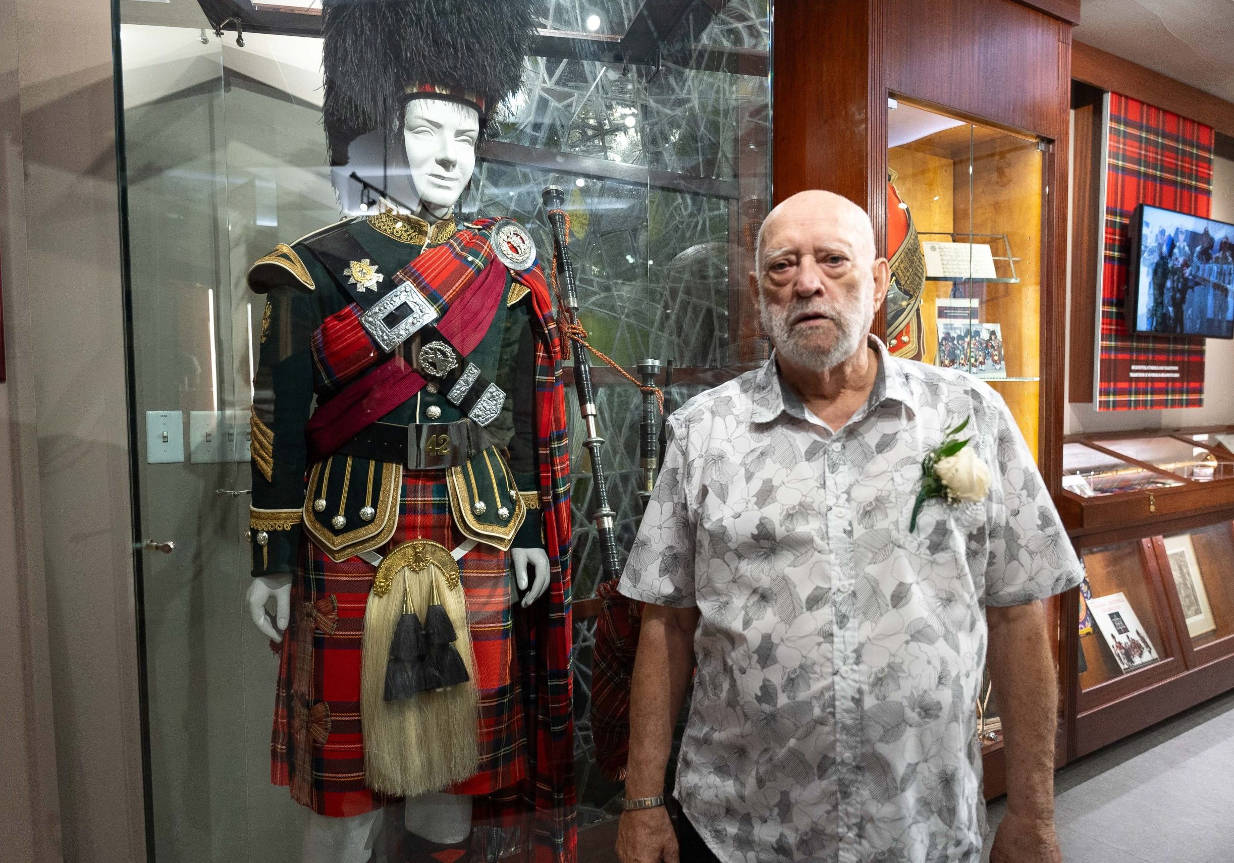 Raymond is posing in front of a display case that is showing the costume of Highland regiment